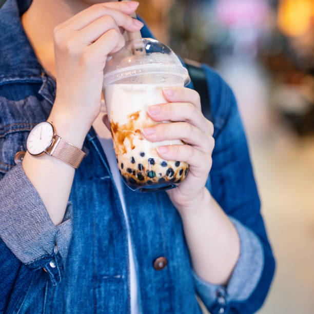 istock Young girl in denim jacket is drinking brown sugar flavored tapioca pearl bubble milk tea with glass straw in night market of Taiwan. 1175236511