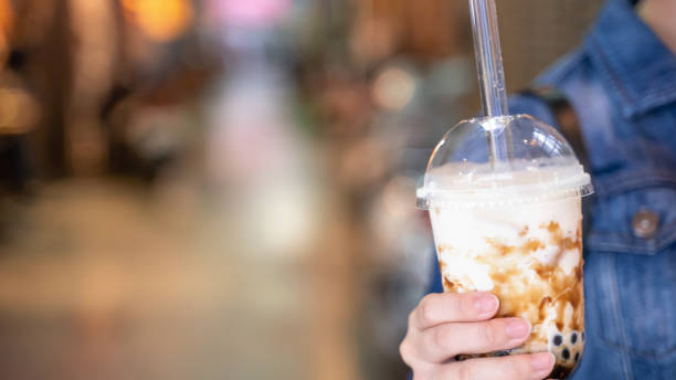 istock Young girl in denim jacket is drinking brown sugar flavored tapioca pearl bubble milk tea with glass straw in night market of Taiwan. 1175236514