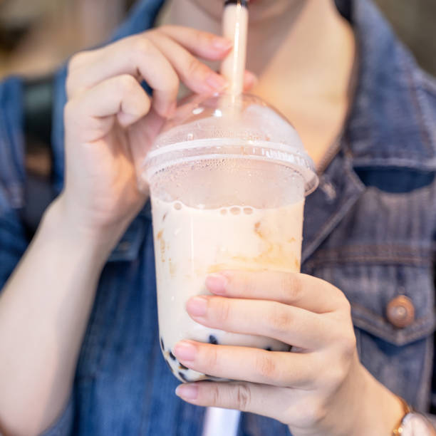 istock Young girl in denim jacket is drinking brown sugar flavored tapioca pearl bubble milk tea with glass straw in night market of Taiwan. 1175236523