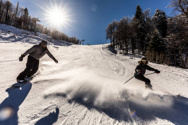 pareja joven divirtiéndose mientras esquiaba por la ladera. - skiing snow couple mountain fotografías e imágenes de stock