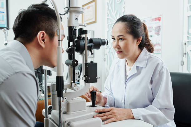 Asian optometrist working at office Asian female optometrist looking through the special medical equipment and examining her patient's eyesight at hospital eye exam stock pictures, royalty-free photos & images