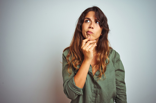 Young beautiful woman wearing green shirt standing over grey isolated background Thinking concentrated about doubt with finger on chin and looking up wondering