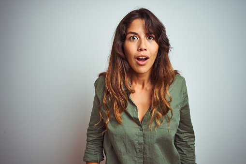 Young beautiful woman wearing green shirt standing over grey isolated background afraid and shocked with surprise and amazed expression, fear and excited face.