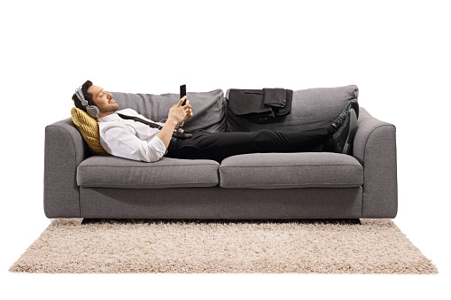 Full length shot of a businessman lying on a sofa and listening to music isolated on white background