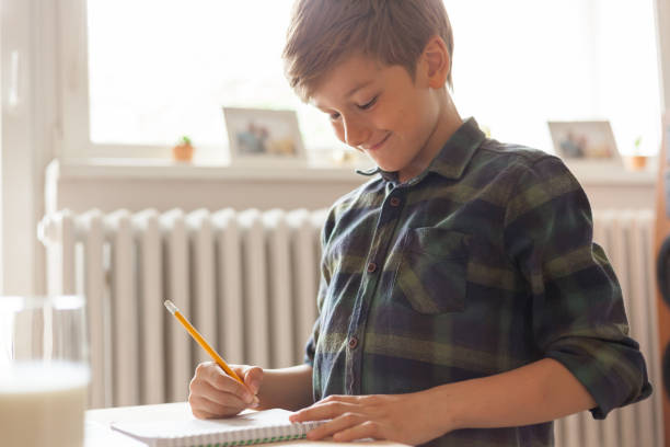 istock Smiling blond hair boy writing to notebook at home 1175241436