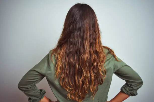 Young beautiful woman wearing green shirt standing over grey isolated background standing backwards looking away with arms on body