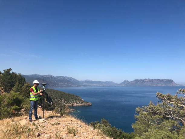 Geodetic engineer surveyor in white hard hat doing measurements with GNSS satellite receiver at the hill top