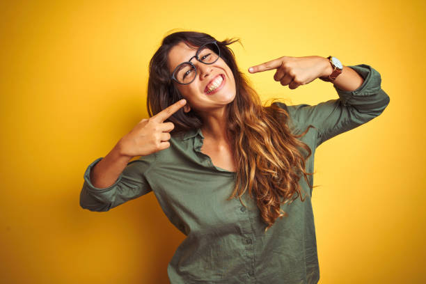 jeune belle femme utilisant la chemise verte et les glaces au-dessus du fond d'isolement de hurlement souriant gai affichant et pointant avec des dents et la bouche de doigts. concept de santé dentaire. - sourire à pleines dents photos et images de collection