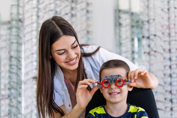 Young smiling boy is sitting and looking at camera through during vision checking. Ophthalmologist is using special medical equipment for eye health saving and improving. Young smiling boy is sitting and looking at camera through during vision checking. Ophthalmologist is using special medical equipment for eye health saving and improving. eye test equipment stock pictures, royalty-free photos & images