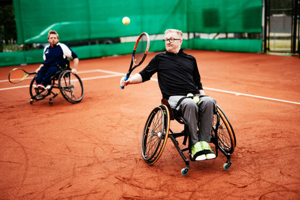 hombres en silla de ruedas jugando al tenis al aire libre - dobles en tierra batida - wheelchair tennis physical impairment athlete fotografías e imágenes de stock
