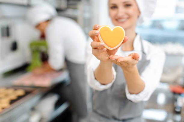 pastelero horneando galletas en forma de corazón - cake women confectioner photography fotografías e imágenes de stock