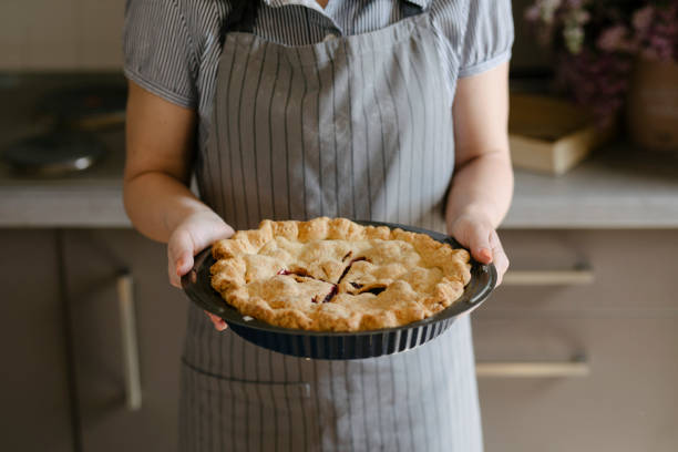 Woman wearing grey apron holding freshly baked apple pie