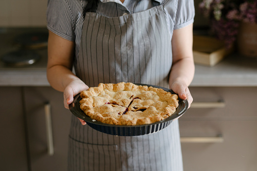 Cropped photo of a young Caucasian woman standing and holding the freshly baked pie.