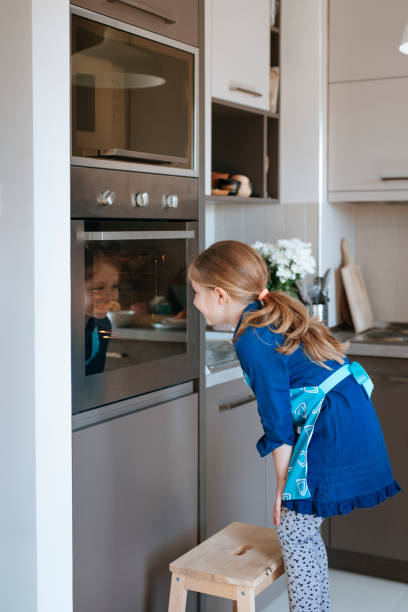 Girl Looking at Her Reflection Caucasian girl looking at her reflection in the oven door glass. oven door stock pictures, royalty-free photos & images