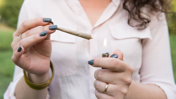 The young person smoking medical marijuana joint outdoors. The young woman smoke cannabis blunt, close-up. Cannabis is a concept of herbal alternative medicine. The young person smoking medical marijuana joint outdoors. The young woman smoke cannabis blunt, close-up. Cannabis is a concept of herbal alternative medicine. cannabaceae stock pictures, royalty-free photos & images