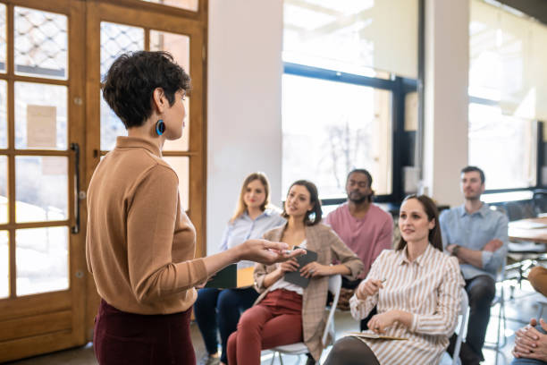 Woman Lecturer Giving Presentation to Businesspeople Pretty stylish woman lecturer giving presentation to a group of businesspeople. small group of people stock pictures, royalty-free photos & images