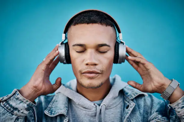 Shot of a handsome young man wearing headphones while posing against a blue background