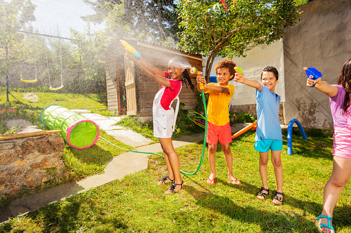 Water gun fight of kids on the backyard shooting with pistol, garden hose spray and squirt