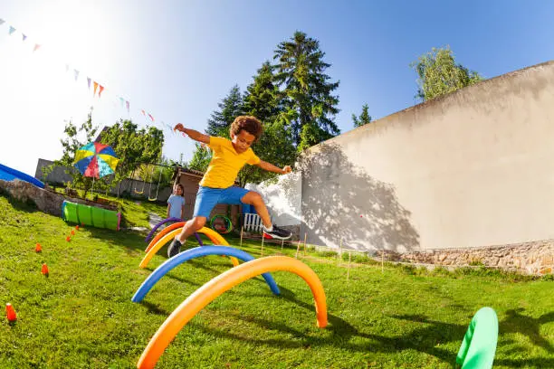 Portrait of a cute curly boy jump over obstacle course barriers playing competition game