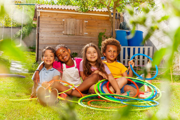 Group of children sit together with hula hoops Group of four children boys, girls sit together holding hula hoops hugging smiling on hot summer day kids play house stock pictures, royalty-free photos & images