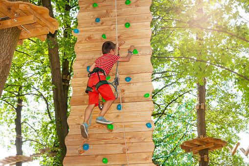 Happy child rock climb on the wooden wall at rope park start