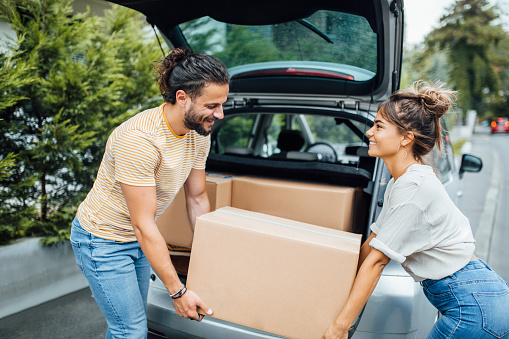 Young millennial couple working together, putting boxes in the back of the car, moving