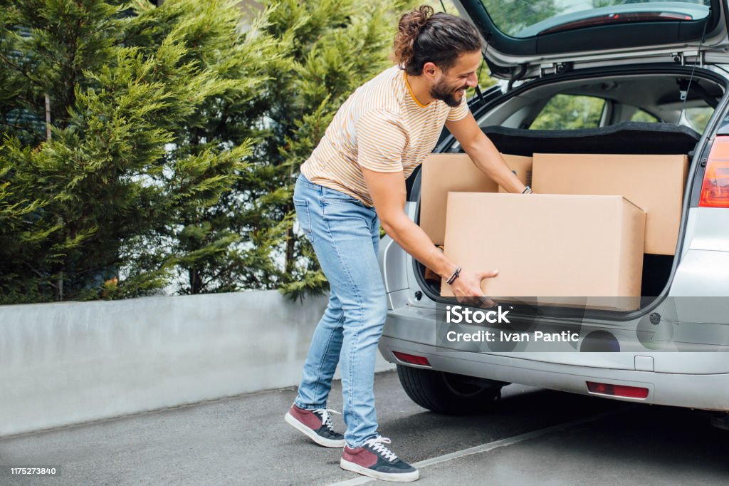 Young millennial man moving away Young millennial man with long hair and a beard, putting boxes in the back of the car, moving Car Stock Photo