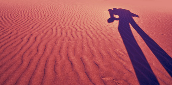 Photographer shadow in sand dunes beach desert wavy texture coral filtered