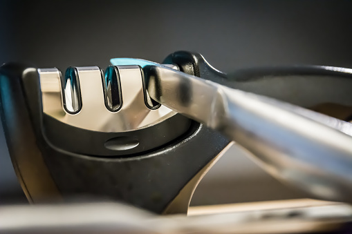 Close-up and detail of a knife in a knife sharpener kitchen tool. Metal and chrome.