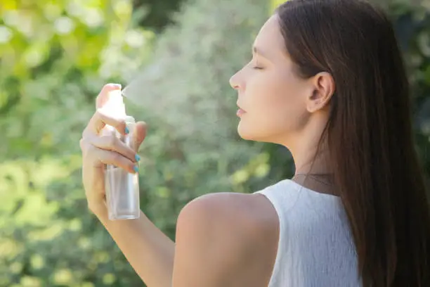 Woman spraying facial mist on her face, summertime skincare concept