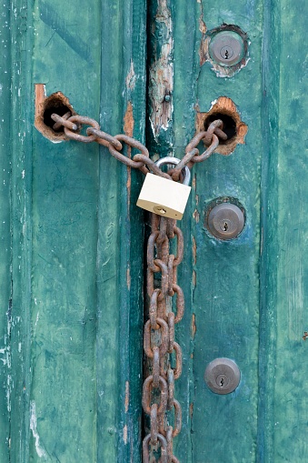 Locks and a padlock and chain on an old house door with peeling paint