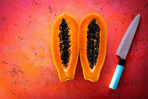 Papaya open in two split knife cut tropical fruit on coral board