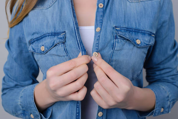 conceito da compra da roupa. foto cortada da mulher que tenta prender a tecla em sua camisa das calças de brim ou desabotoá-la. - shirt close up white button - fotografias e filmes do acervo