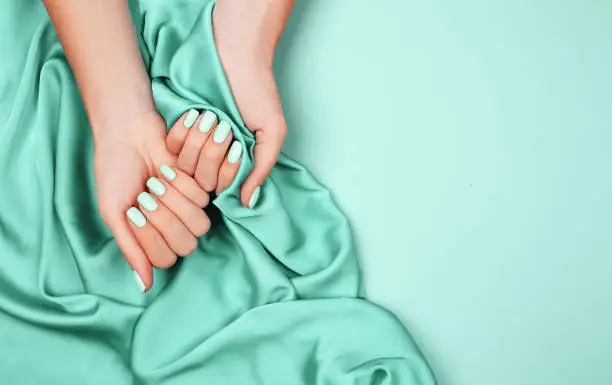 Photo of Hands of a young girl on a mint silk cloth, manicure on a trendy background , green polish.