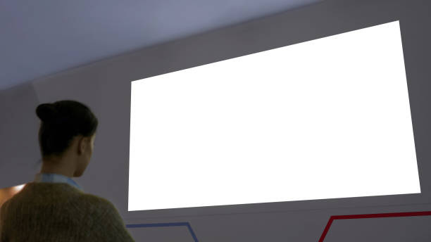 istock Woman looking at large blank white wall screen - cinema mock up 1175304694