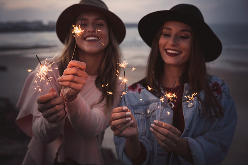 Two beautiful friends celebrating holding sparklers at beach