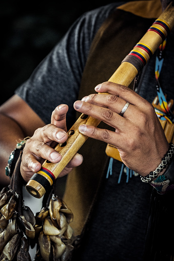 Close-up of Indigenous American musician playing treaditional flute. At the same time he plays the rattle which holding around a wrist.