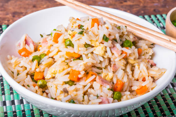 istock Fried rice with egg, ham and vegetables - a traditional Asian dish of fried rice, eggs, ham, carrots and spices in a bowl on a bamboo napkin, chopsticks, close-up 1175313879