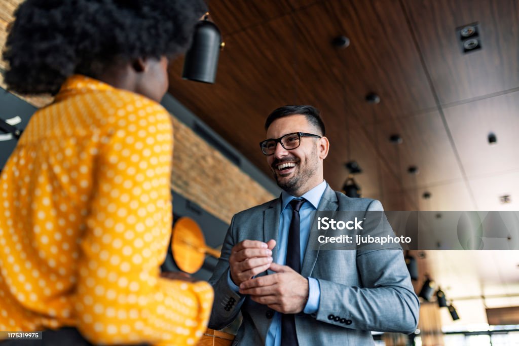 Let's talk business Two happy mixed race Caucasian male and African-American female happy executives meeting in a restaurant and having a business conversation during the day. Greeting Stock Photo