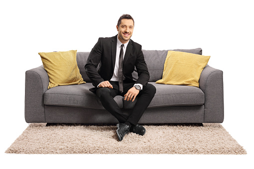 Full length portrait of a businessman sitting on a sofa and smiling isolated on white background