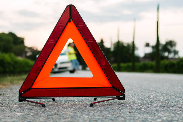 istock Red warning triangle and young man using his mobile phone to call his car assistance. Focus on red triangle! 1175330544