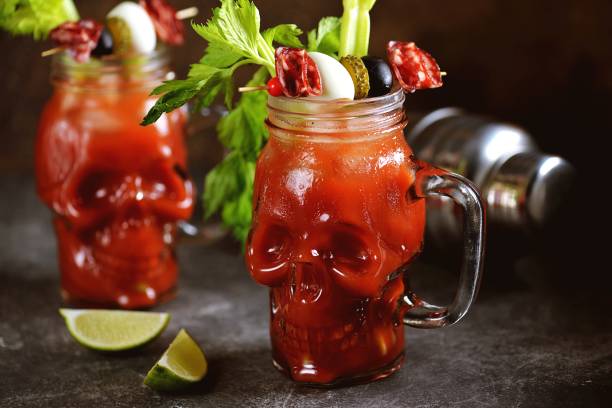 cocktail bloody mary dans le crâne en verre avec des bâtonnets de céleri, sel rose, citron vert et canapes de légumes en conserve. boisson d'halloween. - tomato juice drink celery juice photos et images de collection