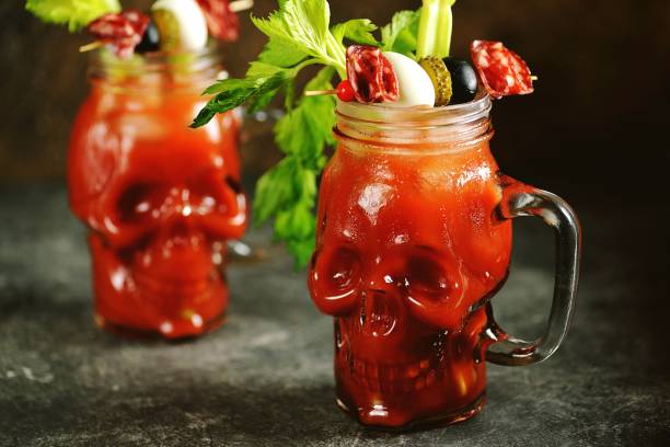 bloody mary cocktail in glass skull with celery sticks, pink salt, lime and canapes from canned vegetables. halloween drink. - bloody mary imagens e fotografias de stock