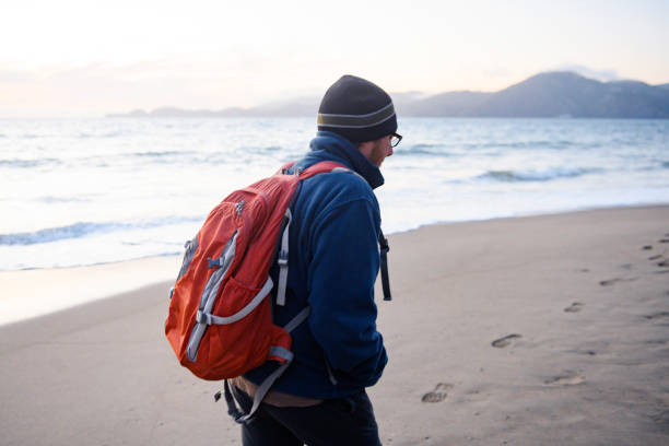 istock Man with Backpack Walking Baker's Beach San Francisco on Cold Afternoon 1175338717