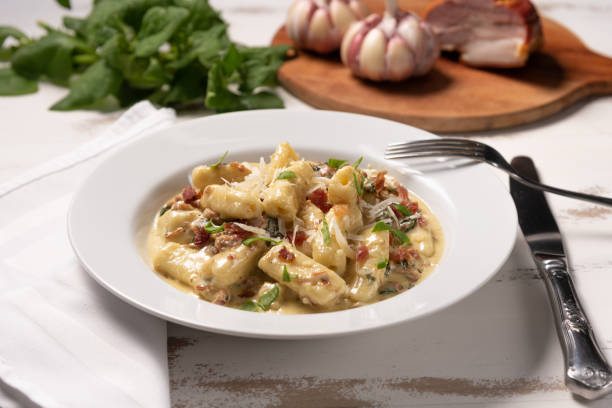 Penne pasta with carbonara sauce in white plate on wooden white background, soft light, angle view. Italian food