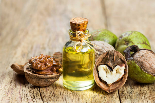 Walnut oil in glass of bottle, whole big peeled walnut kernel with thin shell on wooden background stock photo