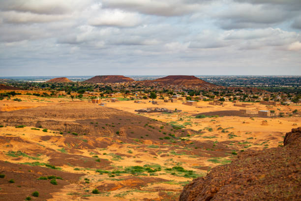 Traditional sahelian mudbrick village with mosque at the foothill of flat-topped hills viewed from a higher plateau with refresehd vegetation during summer rainy season outside Niamey capital of Niger stock photo