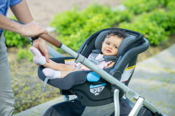 A Latin American man is enjoying a warm afternoon outdoors with his baby daughter. He is pushing the child in a stroller through park. The happy baby is smiling.