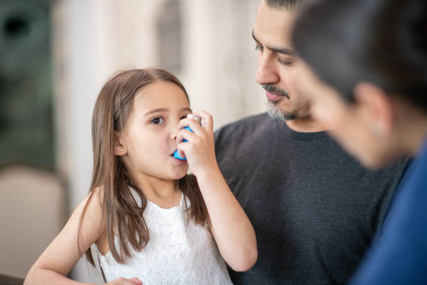 Preschool age girl with asthma learns to use an inhaler A female doctor is showing a preschool age girl how to use an asthma inhaler.  She is talking her through the process. The young girl is sitting on her dads lap who is also listening attentively. asthmatic stock pictures, royalty-free photos & images