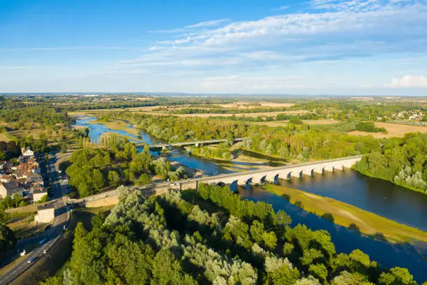 This photo was taken in France, in Burgundy, in the Nièvre, in Guétin towards Nevers. This photo shows the Allier and the Guétin bridge in the middle of the French countryside at the end of the harvest with forests, fields and roads and a blue sky filled with clouds.